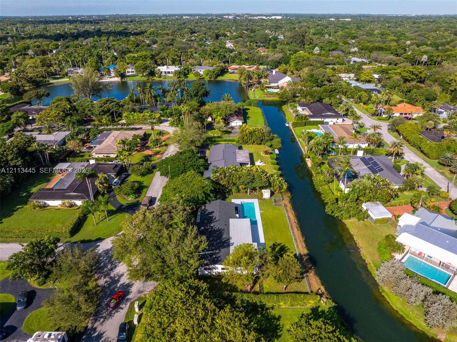 6951 SW 134th Street, Pinecrest, Pinecrest, FL 33156 Aerial perspective of a waterfront property featuring a private swimming pool, a rectangular paved patio, expansive lawn, and direct canal access