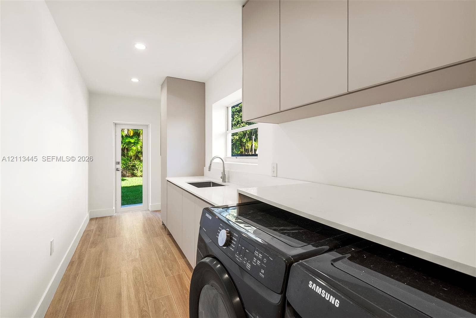 6951 SW 134th Street, Pinecrest, Pinecrest, FL 33156 Utility area featuring flat-panel cabinetry, light-toned stone-finish countertops, an undermount sink with a gooseneck faucet, and wood-finish flooring