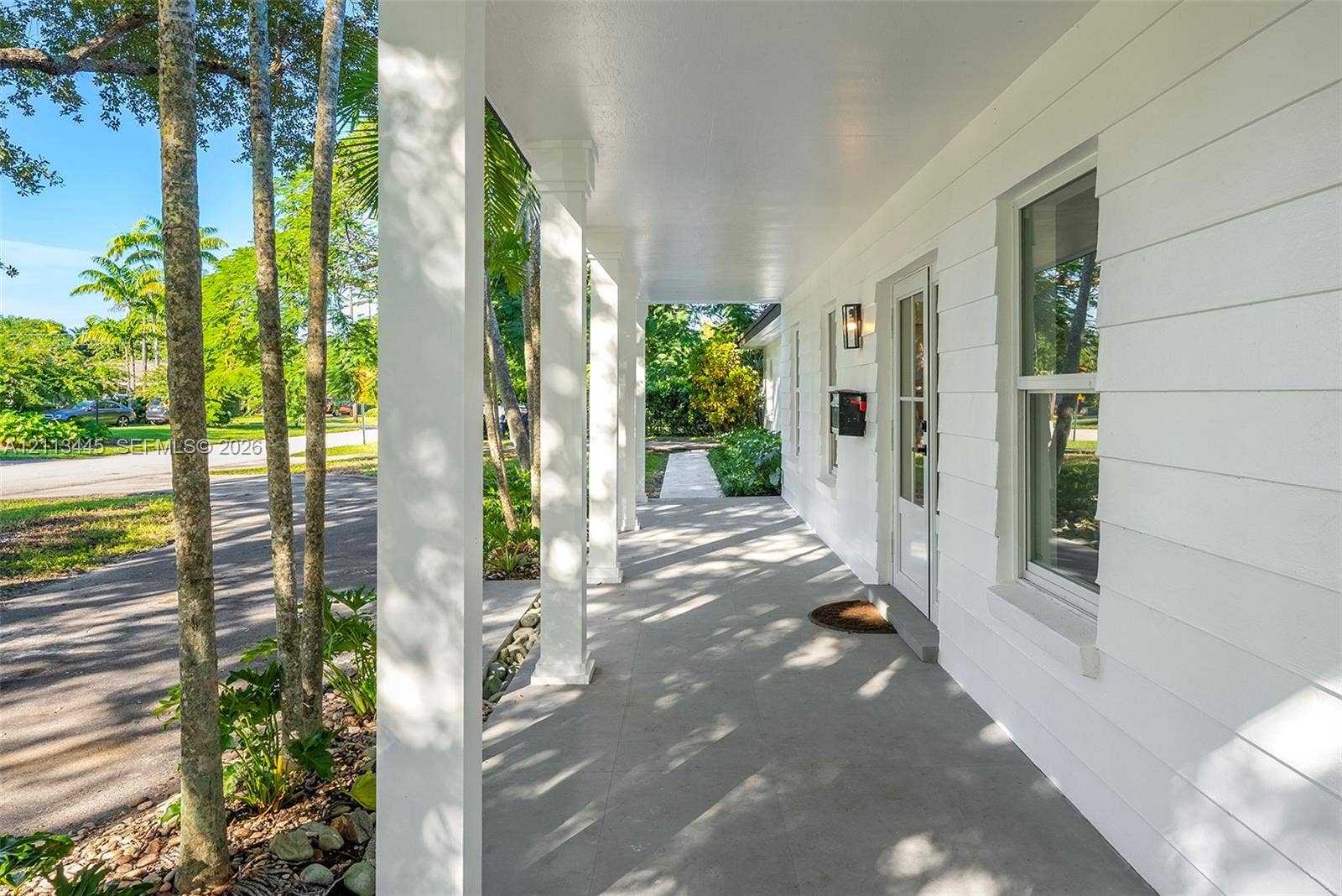 6951 SW 134th Street, Pinecrest, Pinecrest, FL 33156 Covered front porch featuring white horizontal lap siding, square support columns, and a glass-paneled entry door
