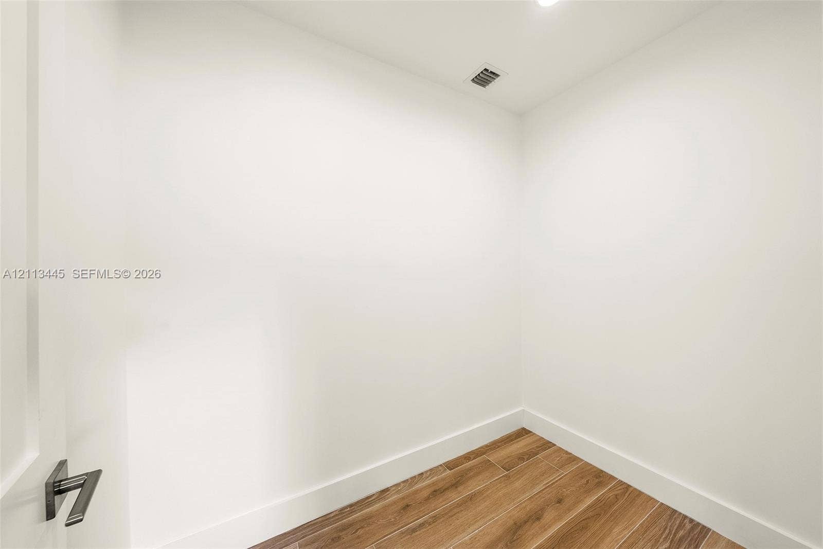 6951 SW 134th Street, Pinecrest, Pinecrest, FL 33156 Interior space featuring white walls and wood-finish flooring with a modern square-profile door handle