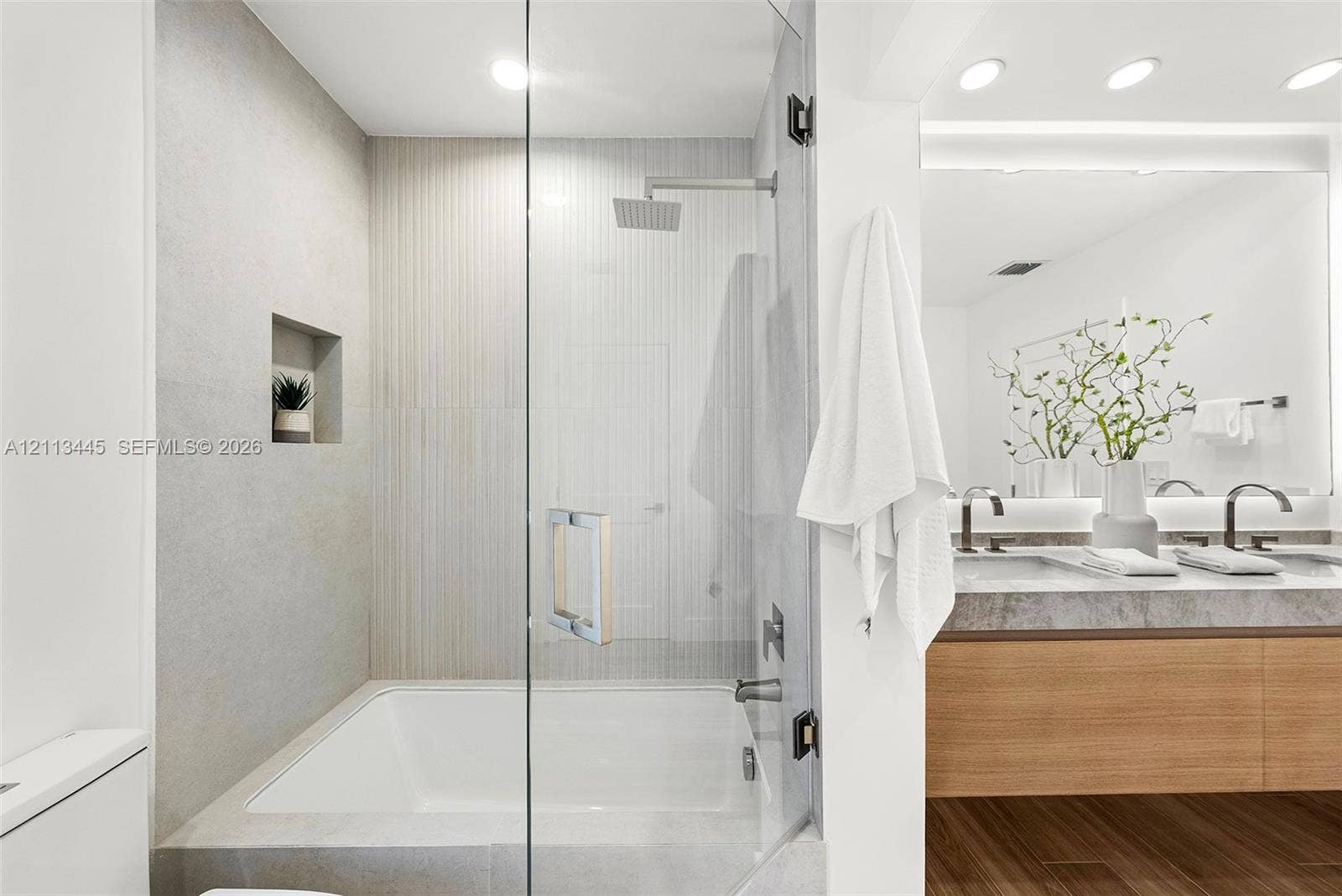 6951 SW 134th Street, Pinecrest, Pinecrest, FL 33156 Shower and tub combination featuring glass enclosure, rain-style shower head, built-in recessed wall niche, dual-sink vanity with stone-finish countertop, and wood-finish flooring