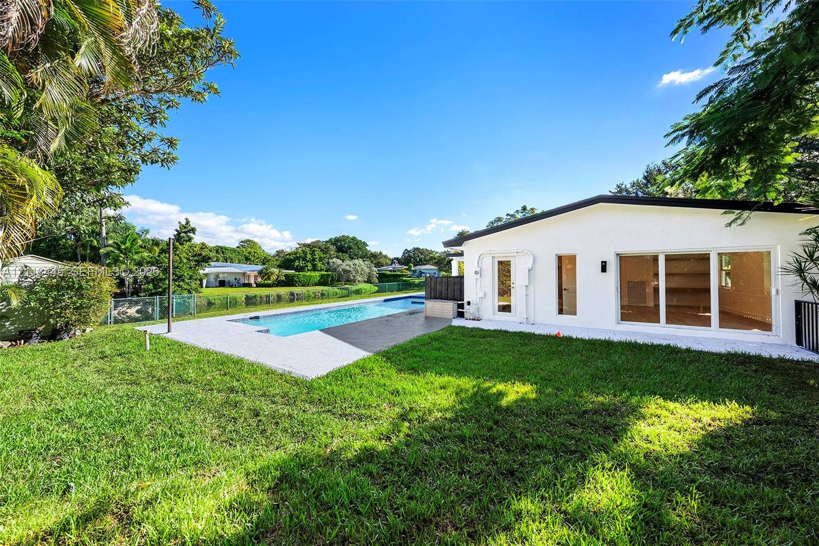 6951 SW 134th Street, Pinecrest, Pinecrest, FL 33156 Backyard featuring an inground swimming pool, concrete pool deck, white stucco exterior, sliding glass doors, and manicured lawn
