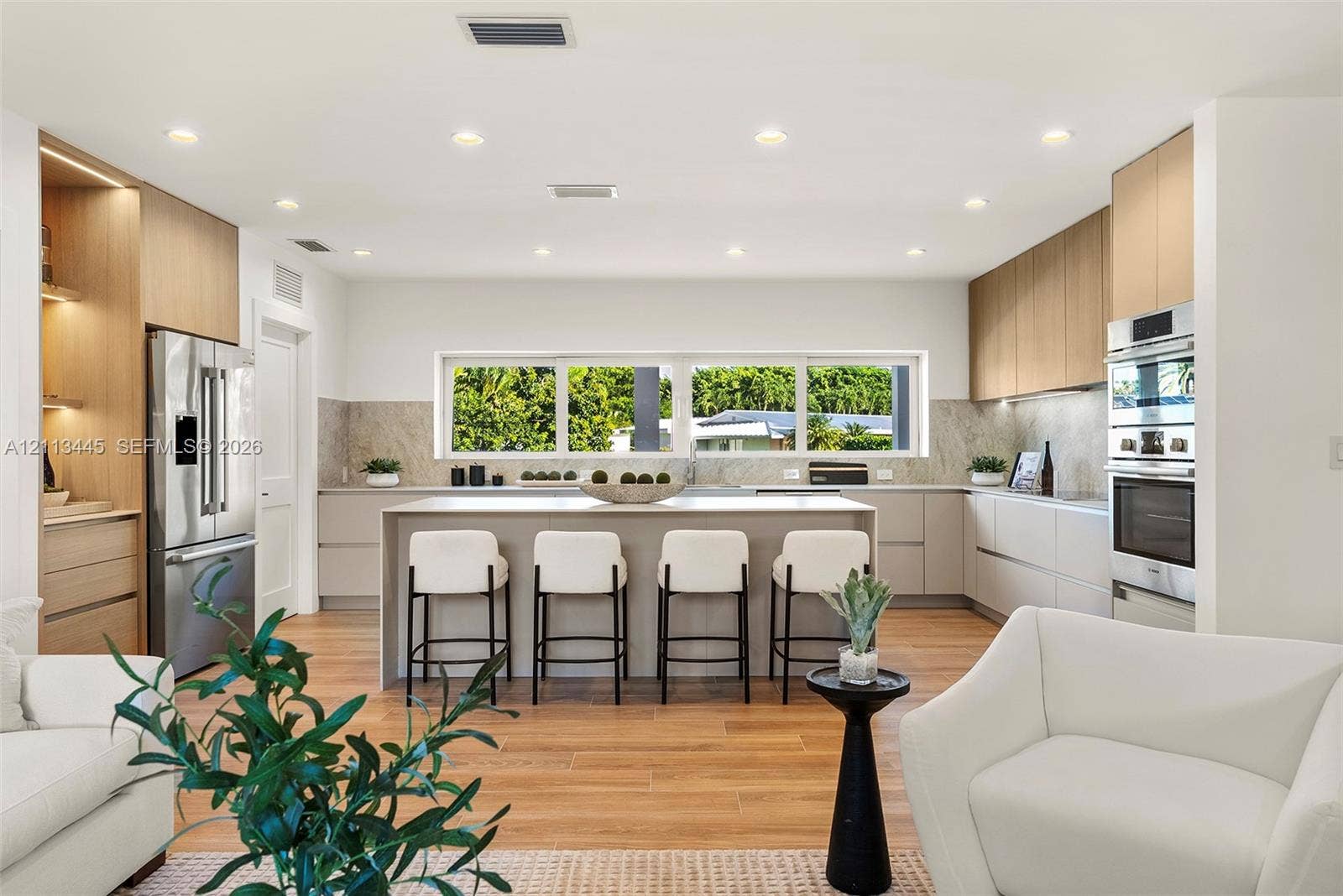 6951 SW 134th Street, Pinecrest, Pinecrest, FL 33156 Modern kitchen featuring light wood-finish cabinetry, a central island with a solid-surface countertop, stainless steel appliances, stone-look backsplash, and recessed lighting