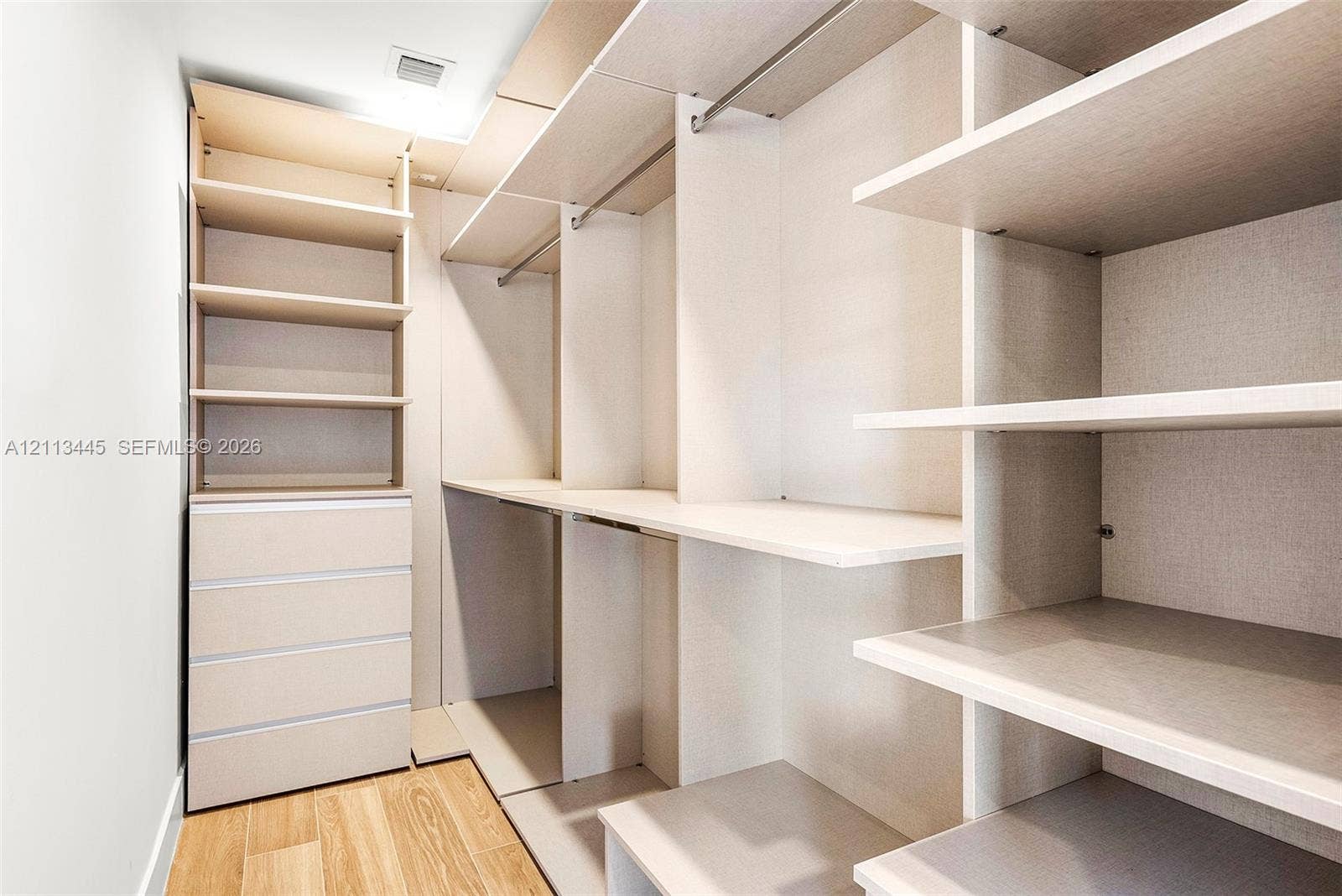 6951 SW 134th Street, Pinecrest, Pinecrest, FL 33156 Walk-in closet featuring custom built-in cabinetry, integrated shelving, multi-level hanging rods, a four-drawer dresser unit, and wood-finish flooring