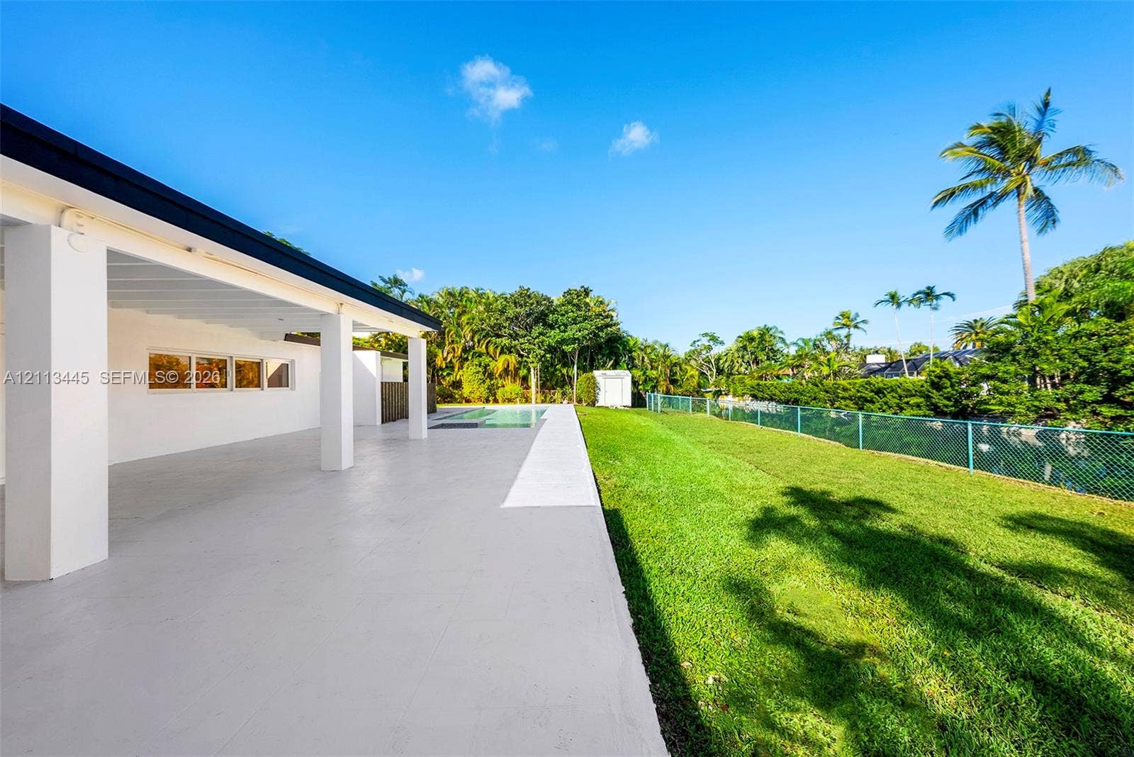 6951 SW 134th Street, Pinecrest, Pinecrest, FL 33156 Covered concrete patio featuring white support columns, inground pool, manicured lawn, and perimeter fencing