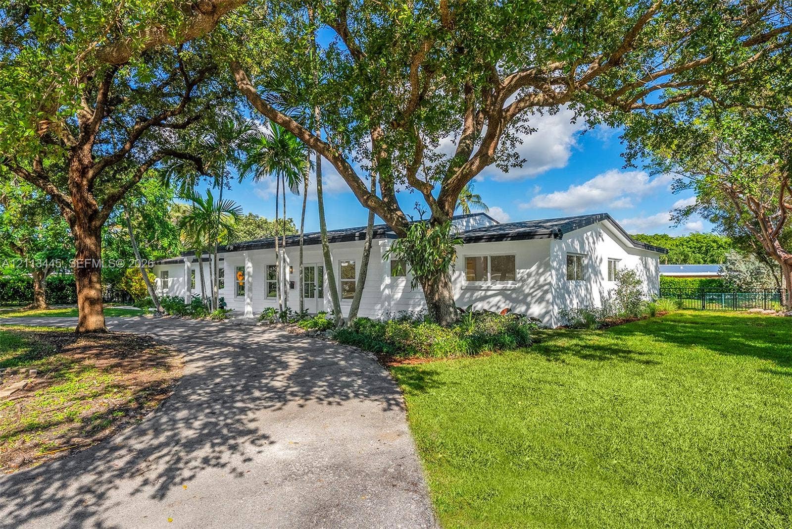 6951 SW 134th Street, Pinecrest, Pinecrest, FL 33156 Single-story exterior featuring a white masonry faade, a paved circular driveway, mature oak trees, and palm landscaping