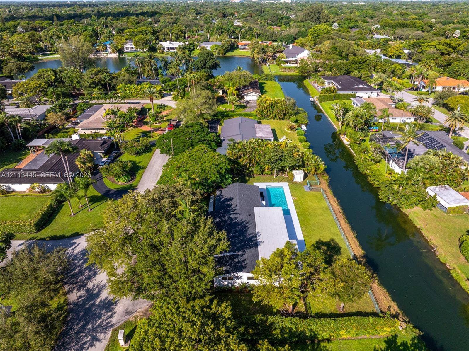 6951 SW 134th Street, Pinecrest, Pinecrest, FL 33156 Aerial perspective of a waterfront property featuring a swimming pool, expansive lawn, mature tree canopy, and canal frontage