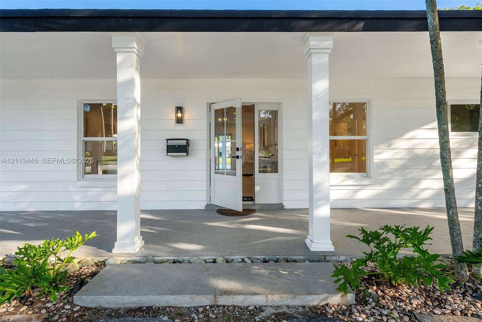 6951 SW 134th Street, Pinecrest, Pinecrest, FL 33156 Covered front porch featuring white horizontal siding, square columns, a concrete foundation, and a glass-paneled entry door