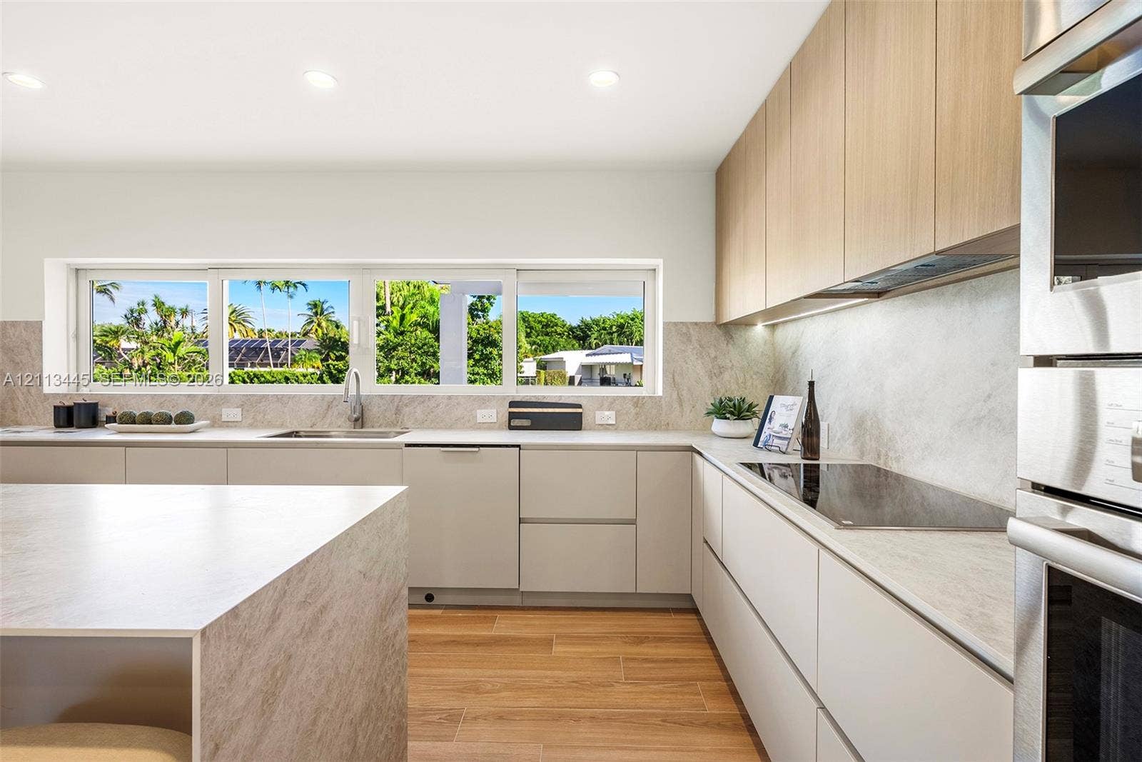6951 SW 134th Street, Pinecrest, Pinecrest, FL 33156 Kitchen featuring flat-panel cabinetry, wood-finish flooring, stone-finish countertops and backsplash, integrated stainless steel appliances, and a horizontal window
