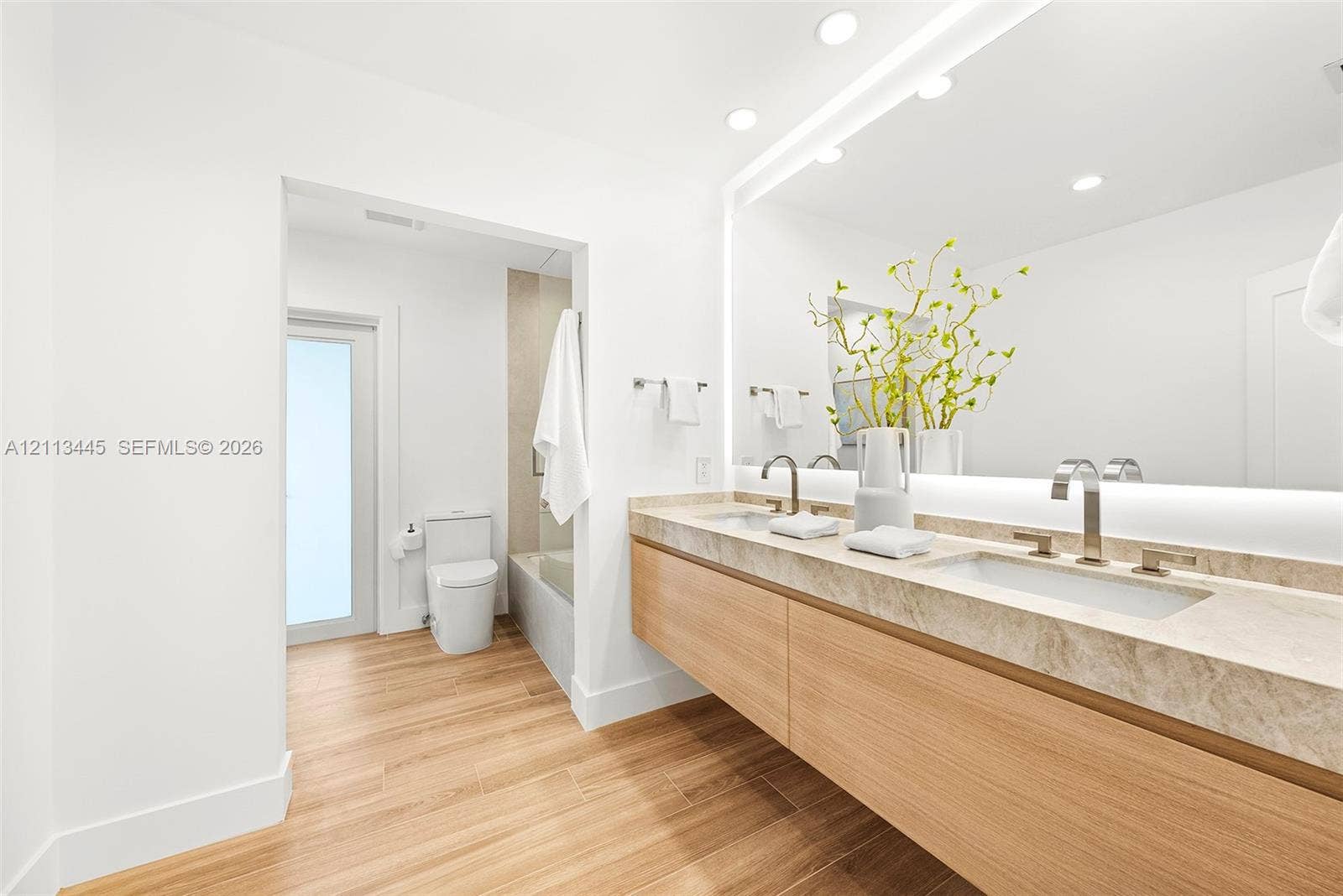 6951 SW 134th Street, Pinecrest, Pinecrest, FL 33156 Floating dual vanity with stone countertop, under-mount sinks, modern metal faucets, wood-finish cabinetry, and oversized wall-mounted LED mirror