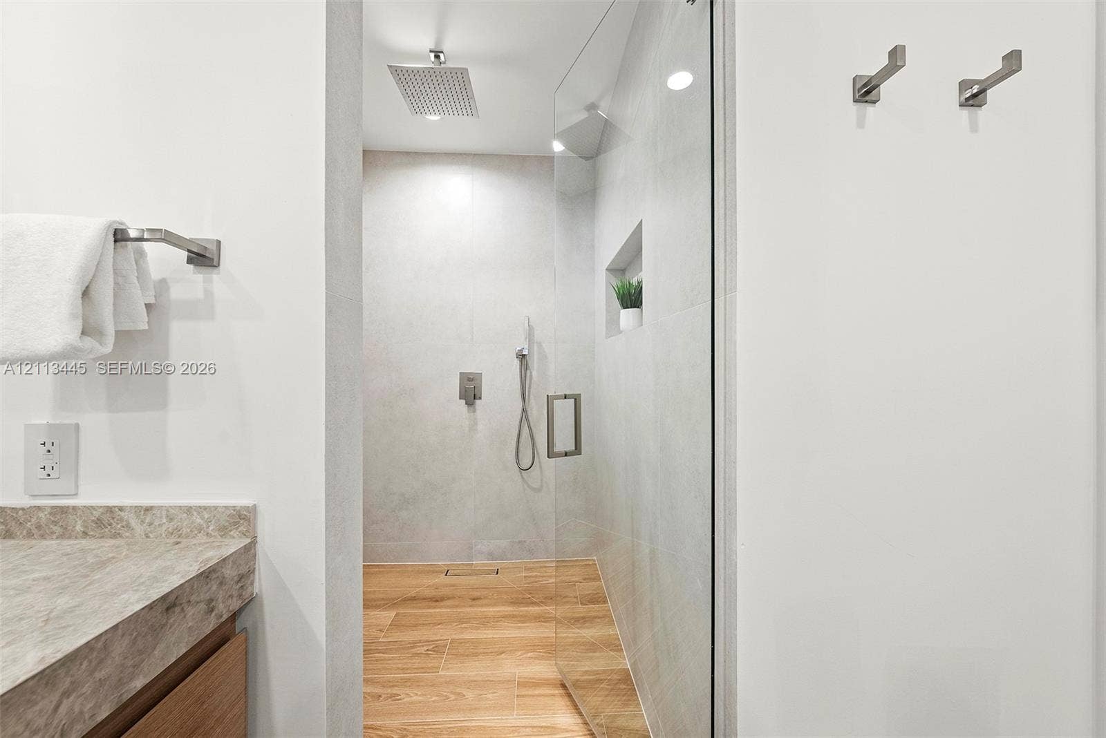 6951 SW 134th Street, Pinecrest, Pinecrest, FL 33156 Walk-in shower featuring glass enclosure, ceiling-mounted rainfall showerhead, handheld sprayer, integrated wall niche, and wood-finish flooring