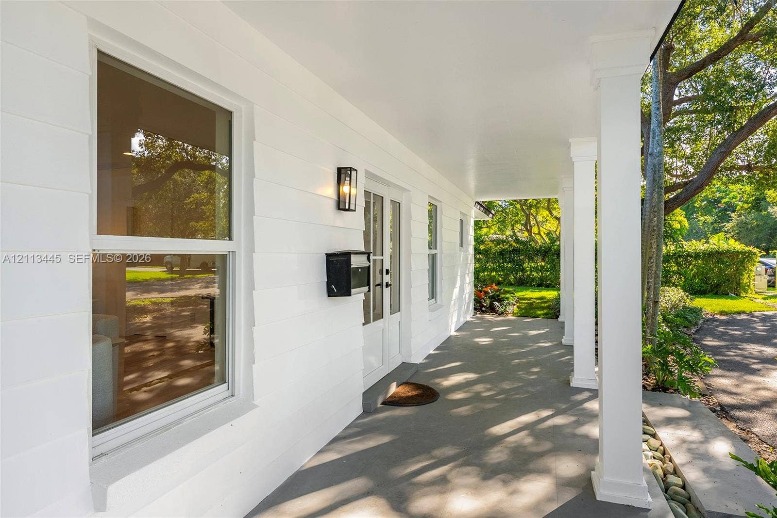 6951 SW 134th Street, Pinecrest, Pinecrest, FL 33156 Covered front porch featuring smooth-finish ceiling, square structural columns, horizontal lap siding, wall-mounted exterior lighting, and double-entry doors