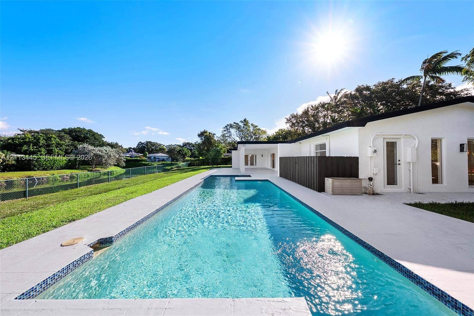 6951 SW 134th Street, Pinecrest, Pinecrest, FL 33156 Rectangular in-ground swimming pool with mosaic tile border, light-toned stone pool deck, and manicured grass grounds