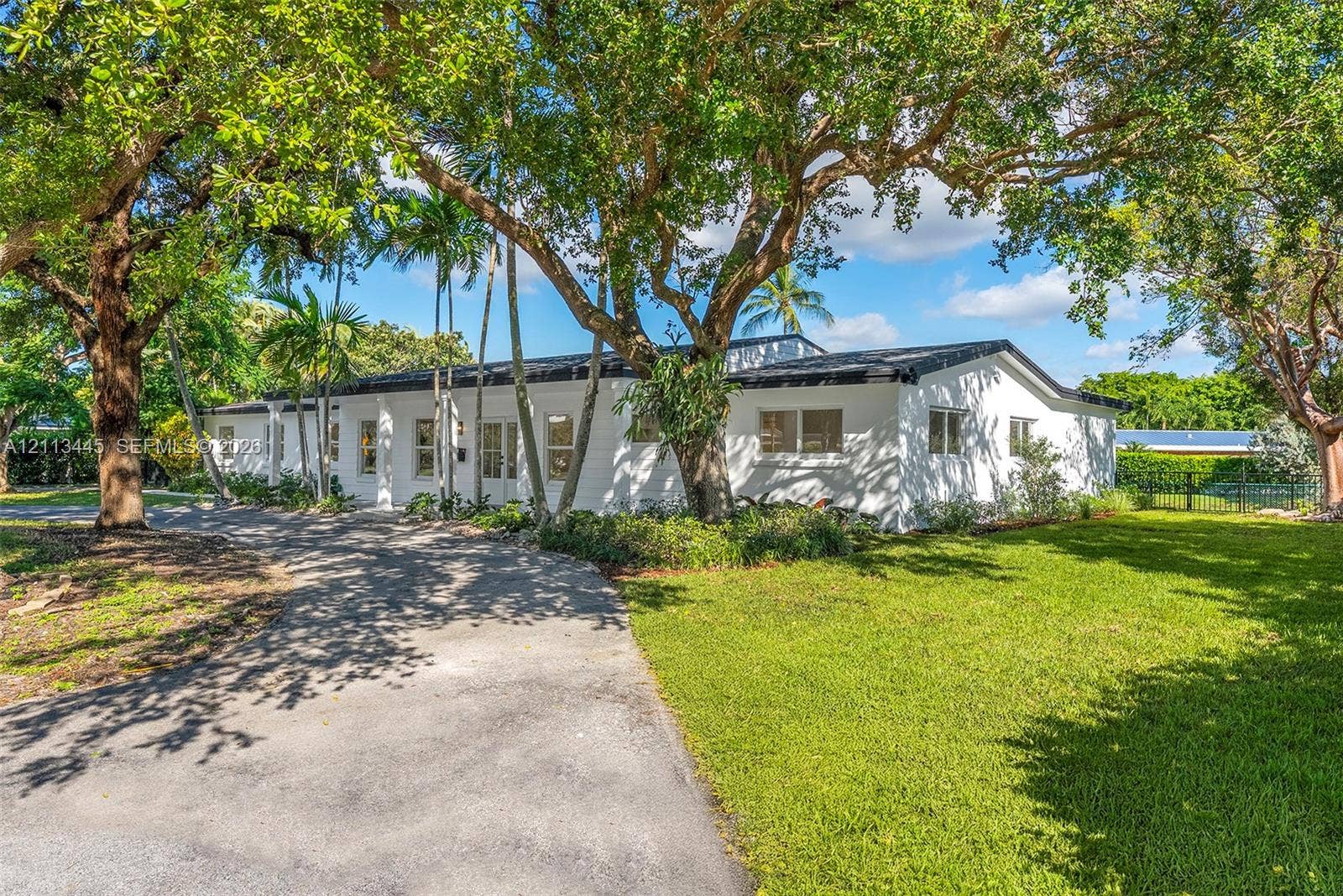 6951 SW 134th Street, Pinecrest, Pinecrest, FL 33156 Single-story exterior featuring white masonry walls, a flat roofline, paved driveway, and mature landscaping