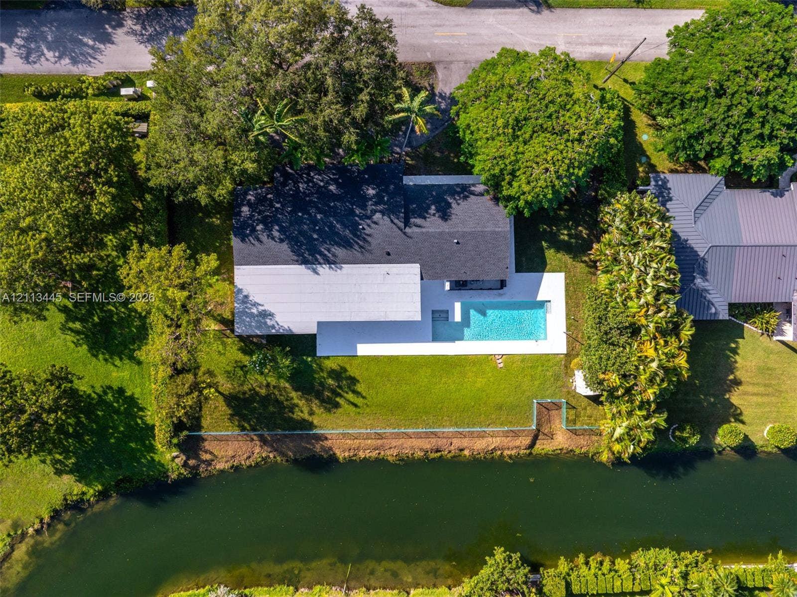 6951 SW 134th Street, Pinecrest, Pinecrest, FL 33156 Aerial perspective featuring a waterfront property with an in-ground swimming pool, concrete pool deck, expansive lawn, and mature landscaping