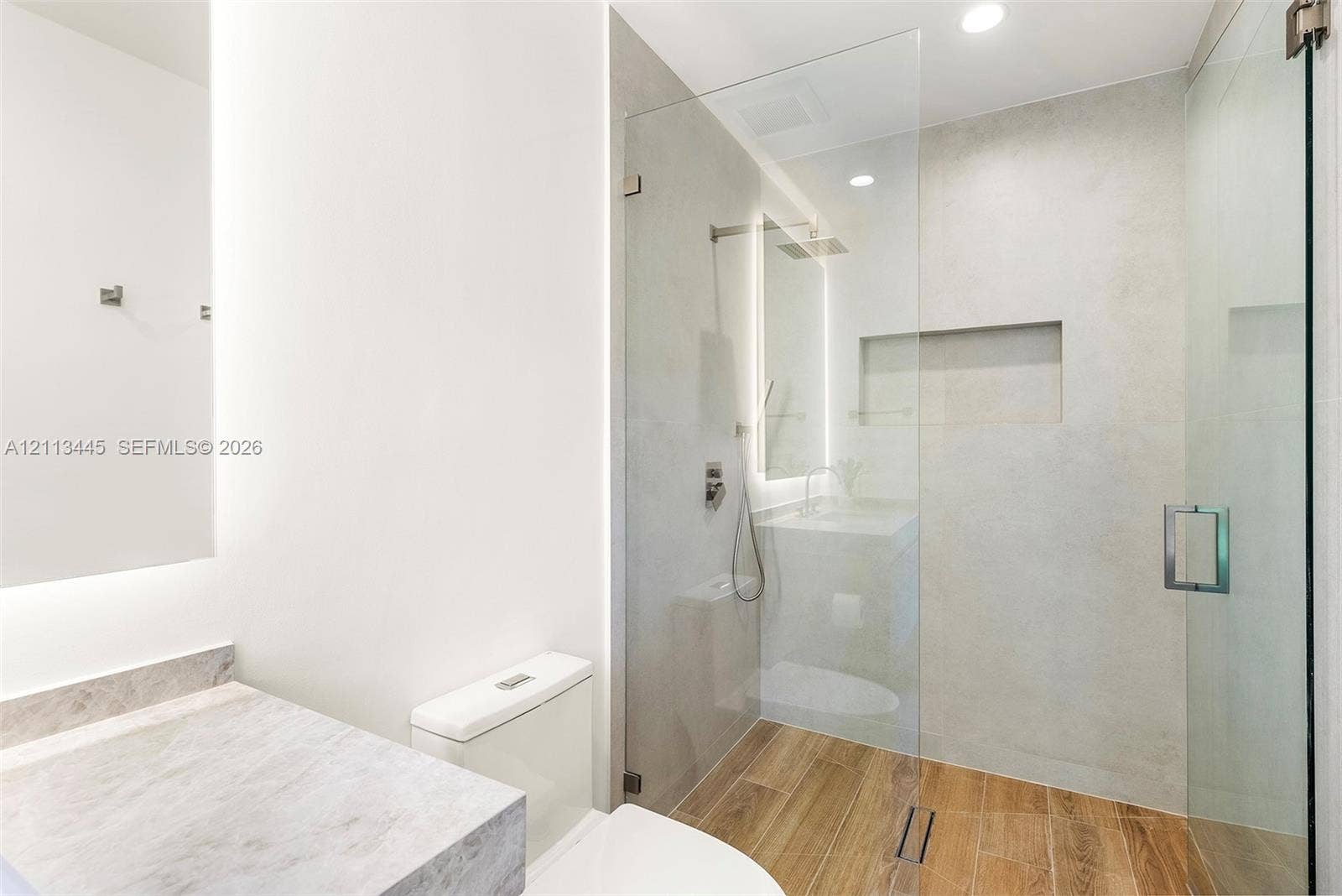 6951 SW 134th Street, Pinecrest, Pinecrest, FL 33156 Bathroom featuring a frameless glass shower enclosure, wood-finish flooring, integrated wall niche, stone-look countertop, and recessed LED lighting
