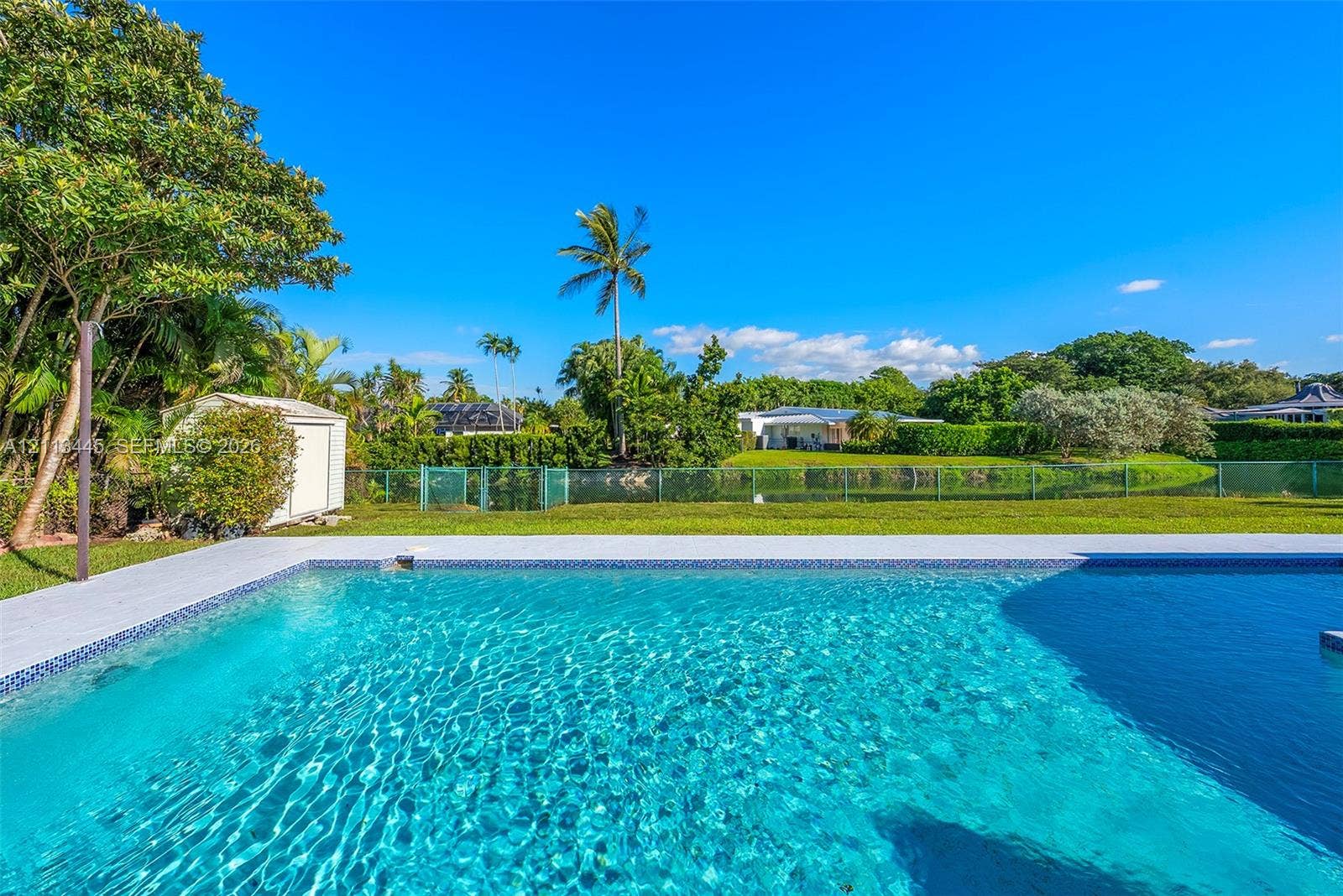 6951 SW 134th Street, Pinecrest, Pinecrest, FL 33156 In-ground swimming pool with light-colored coping, surrounded by a paved deck, green lawn, and mature perimeter landscaping