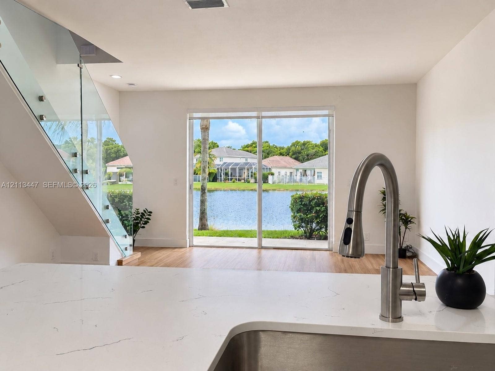 3818 San Simeon Circle, #3818, Weston, Weston, FL 33331 Kitchen featuring white Carrara quartz countertops, stainless steel undermount sink with arched pull-down faucet, glass-panel staircase railing, and sliding glass doors leading to water-side exterior