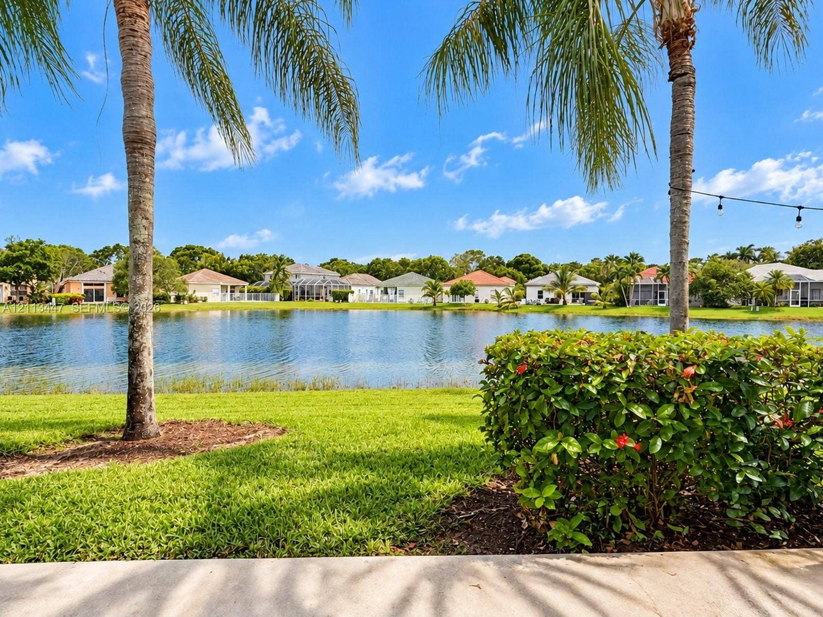 3818 San Simeon Circle, #3818, Weston, Weston, FL 33331 Waterfront backyard featuring a manicured lawn, established palm trees, mature shrubbery, and a concrete patio
