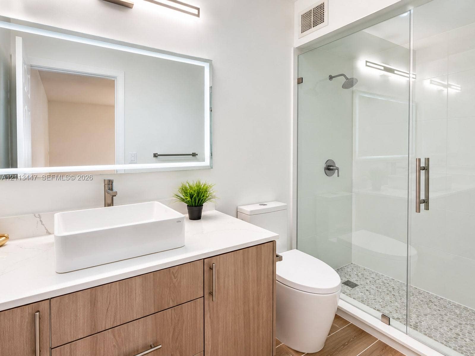 3818 San Simeon Circle, #3818, Weston, Weston, FL 33331 Bathroom featuring a wood-finish vanity with a stone-top counter, white vessel sink, rectangular LED-backlit mirror, and a walk-in shower with a glass enclosure and stone tile flooring