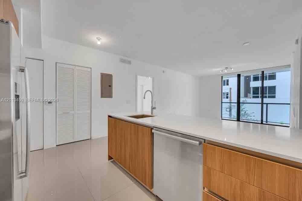 Kitchen featuring a quartz-topped island, light wood-finish cabinetry, stainless steel dishwasher, undermount sink with a gooseneck faucet, and polished tile flooring