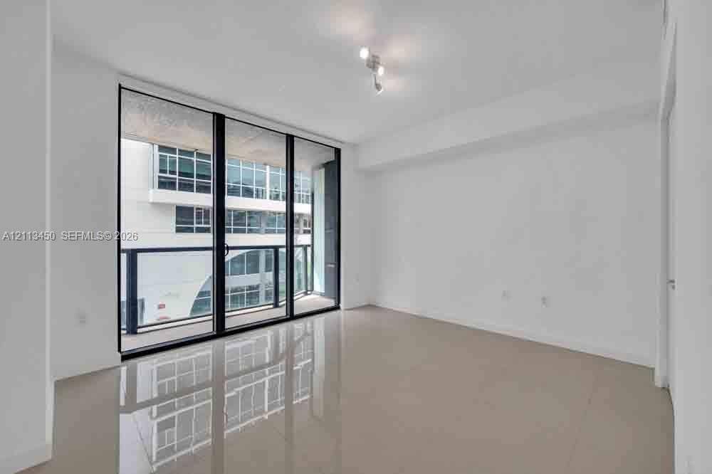 Floor-to-ceiling glass sliding doors, private balcony with metal railing, smooth-finish flooring, and minimalist track lighting