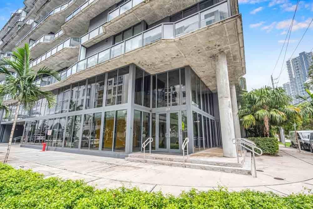 Contemporary multi-story exterior featuring floor-to-ceiling glass paneling, exposed concrete soffits, wrap-around glass balconies, and structural column supports