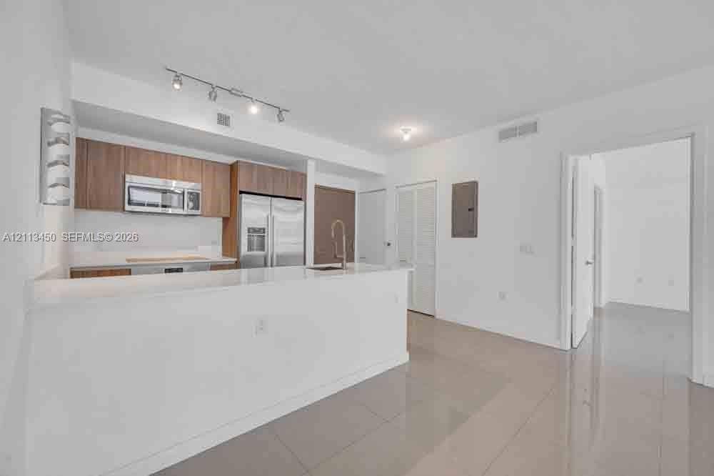 Kitchen featuring wood-finish cabinetry, white countertop, stainless steel appliances, track lighting, and tile flooring
