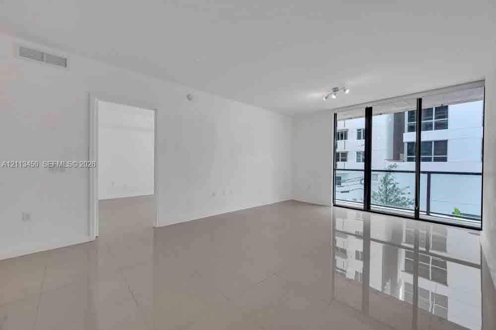 Interior space featuring large-format tile flooring, floor-to-ceiling glass paneling, and access to an exterior balcony