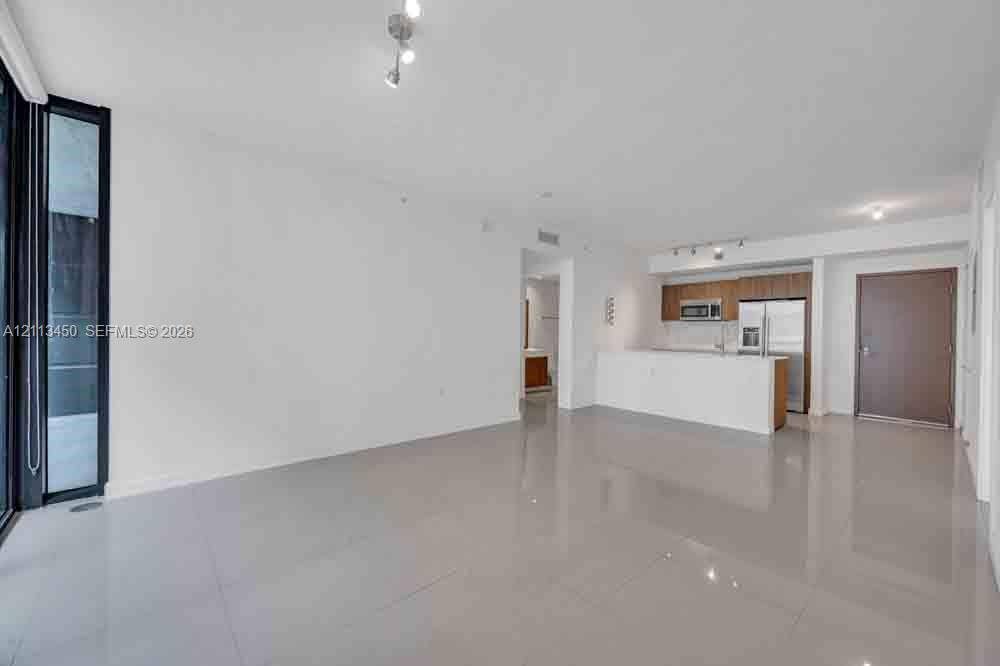 Open-concept main living area with large-format tile flooring, kitchen featuring wood-finish cabinetry, white countertop peninsula, and stainless steel appliances