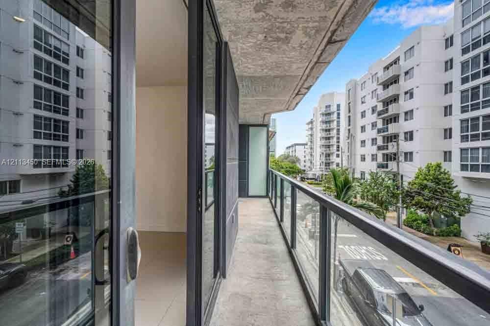 Covered balcony with a concrete ceiling, glass panel railing, and full-height sliding glass door entry