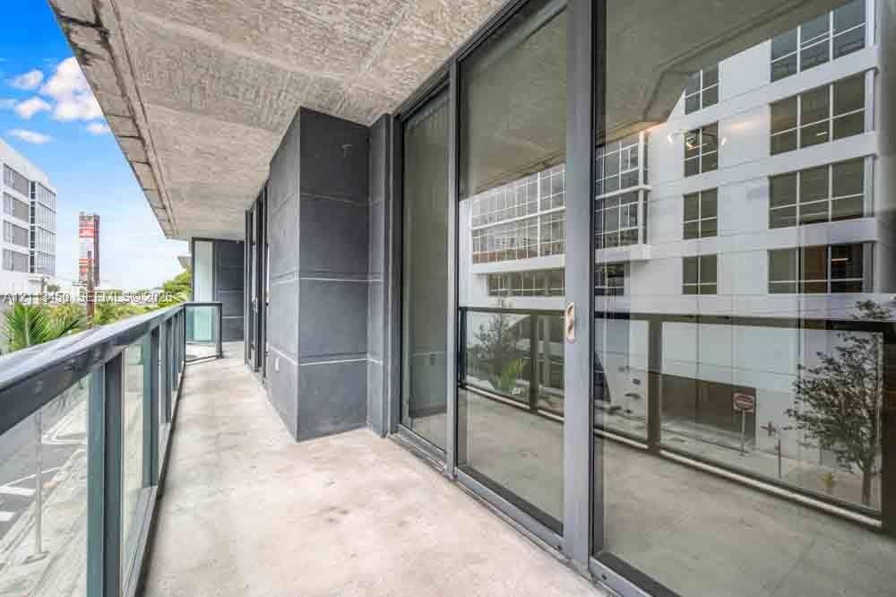 Covered private balcony featuring concrete flooring, charcoal-toned structural columns, and a glass-paneled railing system with full-height sliding glass doors