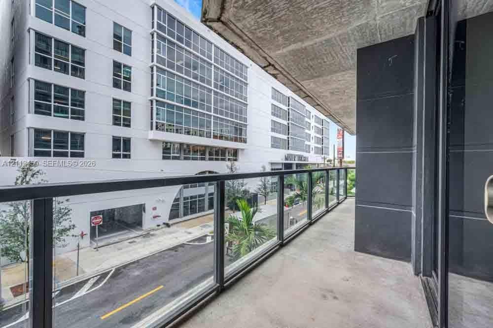Covered balcony featuring concrete flooring, charcoal-toned vertical wall cladding, and a frameless glass railing system