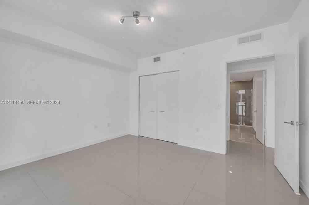 Neutral-toned tile flooring, recessed multi-directional lighting fixture, and white double-door closet cabinetry