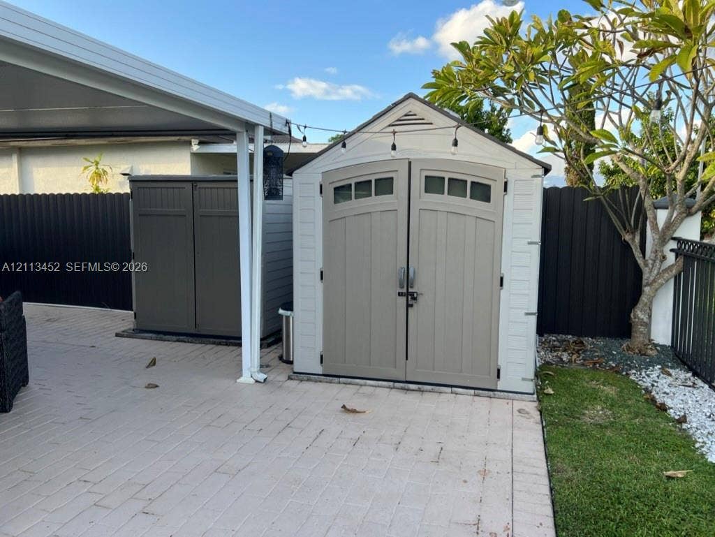 5083 SW 160th Avenue, Miami, Miami, FL 33185 Exterior storage shed featuring dual entry doors, transom windows, and a neutral finish, situated on a paved patio surface