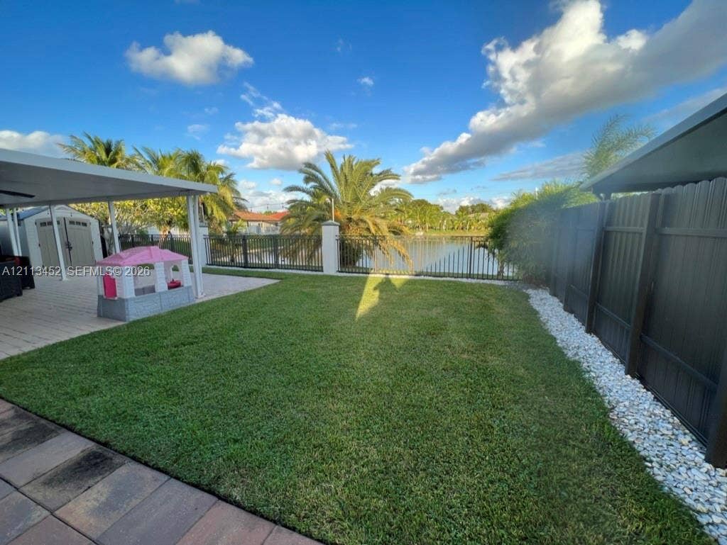 5083 SW 160th Avenue, Miami, Miami, FL 33185 Rear yard featuring a covered patio, paved hardscaping, manicured lawn, dark metal fencing, and stone landscape bordering