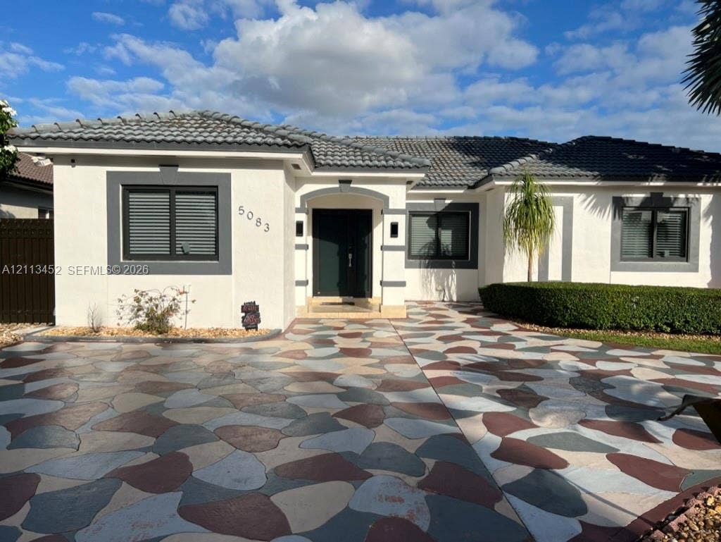 5083 SW 160th Avenue, Miami, Miami, FL 33185 Stucco exterior featuring dark-toned window trim, a multi-colored stone-pattern driveway, a recessed entryway, and a low-profile tile roof