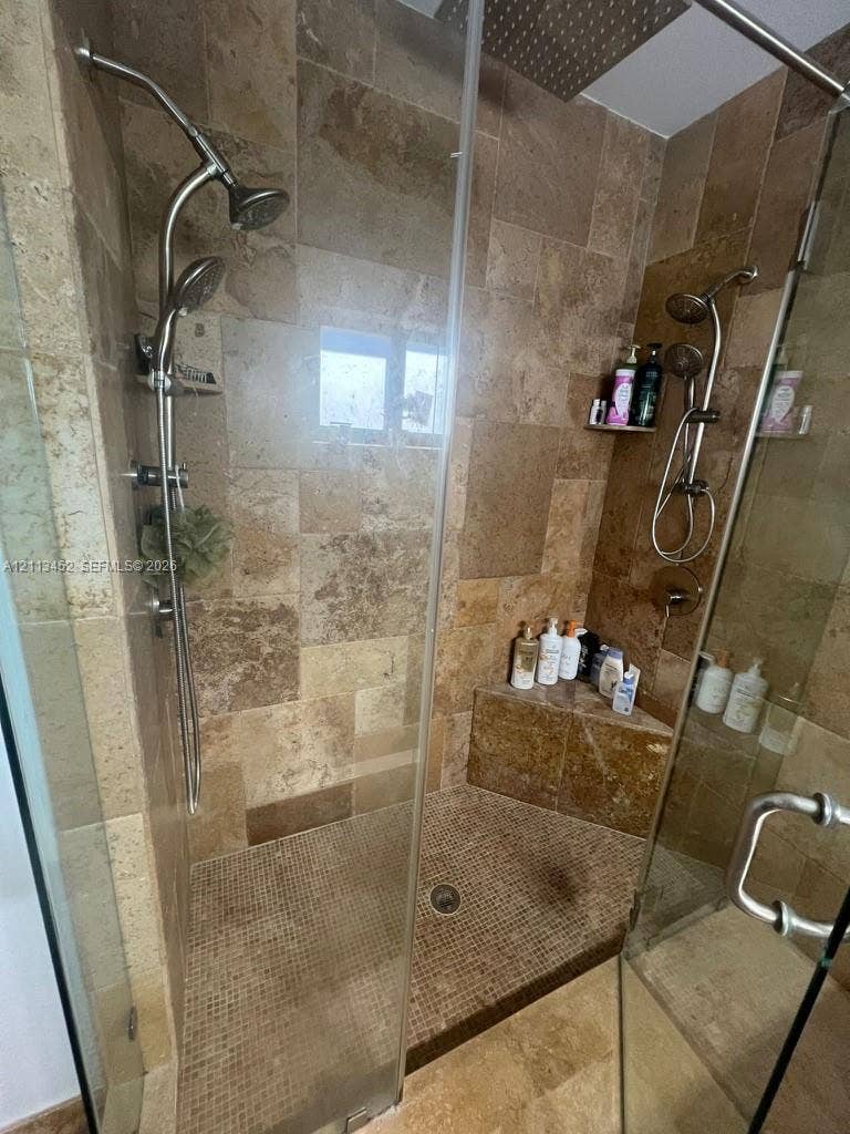 5083 SW 160th Avenue, Miami, Miami, FL 33185 Walk-in shower featuring natural stone wall tile, mosaic tile flooring, built-in corner bench, dual adjustable handheld showerheads, and frameless glass enclosure