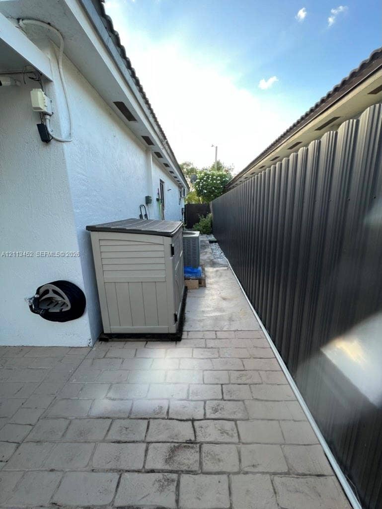 5083 SW 160th Avenue, Miami, Miami, FL 33185 Side yard featuring light-toned concrete paver hardscaping and a tall dark-finished corrugated metal privacy fence