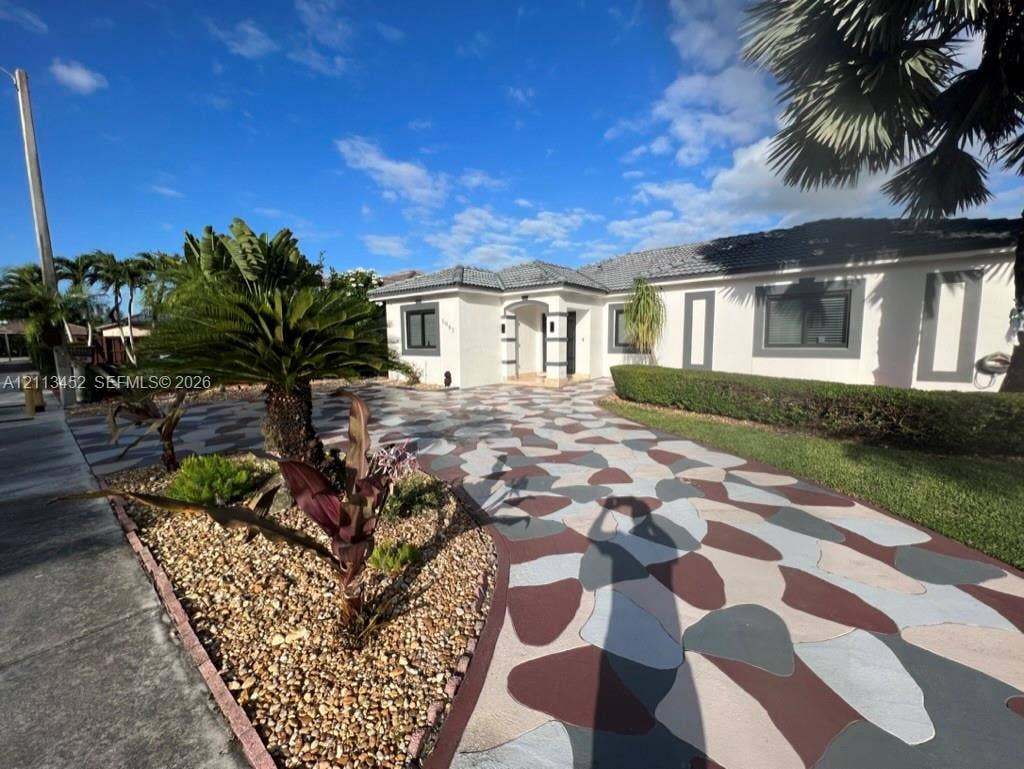 5083 SW 160th Avenue, Miami, Miami, FL 33185 Single-story exterior featuring a decorative stone-pattern driveway, concrete facade, hipped tile roof, and landscaped garden beds with established tropical flora