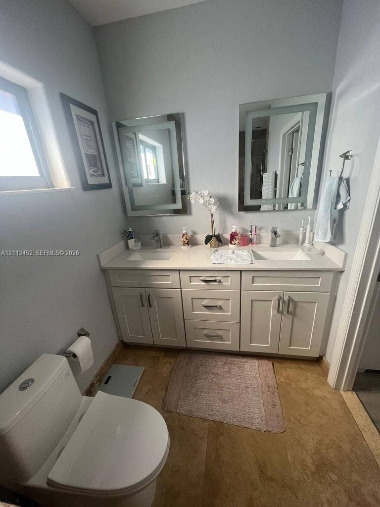 5083 SW 160th Avenue, Miami, Miami, FL 33185 Dual-sink vanity with white shaker-style cabinetry, solid-surface countertop, integrated rectangular basins, and dual lighted wall-mounted mirrors, complemented by stone-finish flooring