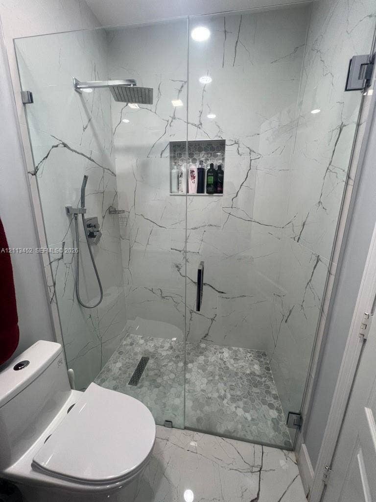 5083 SW 160th Avenue, Miami, Miami, FL 33185 Walk-in shower featuring large-format veined tile surround, frameless glass enclosure, rainfall showerhead with handheld attachment, recessed tile niche, and textured pebble floor tiling with a linear drain
