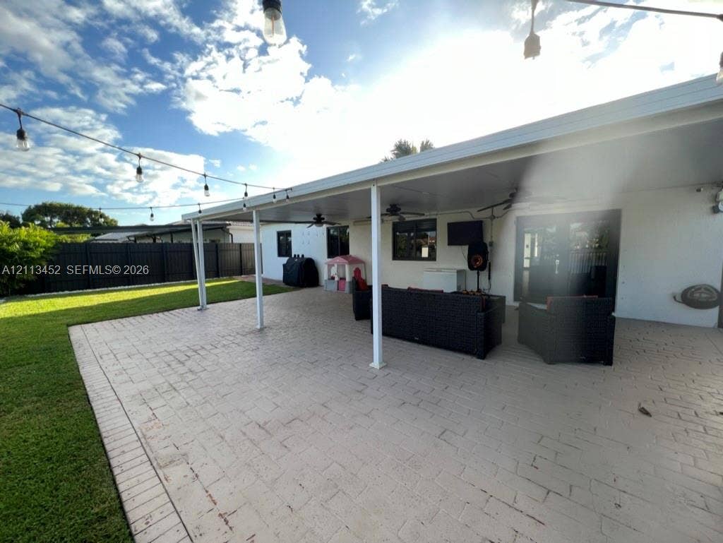 5083 SW 160th Avenue, Miami, Miami, FL 33185 Covered outdoor patio featuring stamped concrete flooring, integrated ceiling fans, overhead string lighting, and a manicured lawn enclosed by perimeter fencing