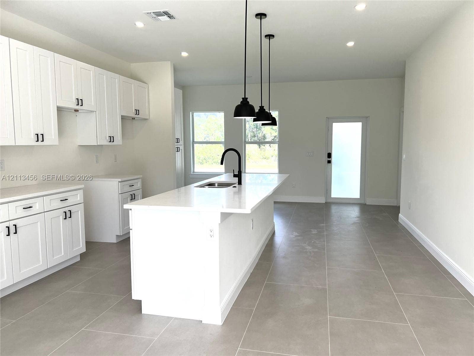 422 SE Eisenhower Boulevard, Lehigh Acres, FL 33974 Kitchen featuring white cabinetry, an expansive center island with a stone-surface countertop, matte black faucet hardware, pendant lighting, and neutral-toned tile flooring