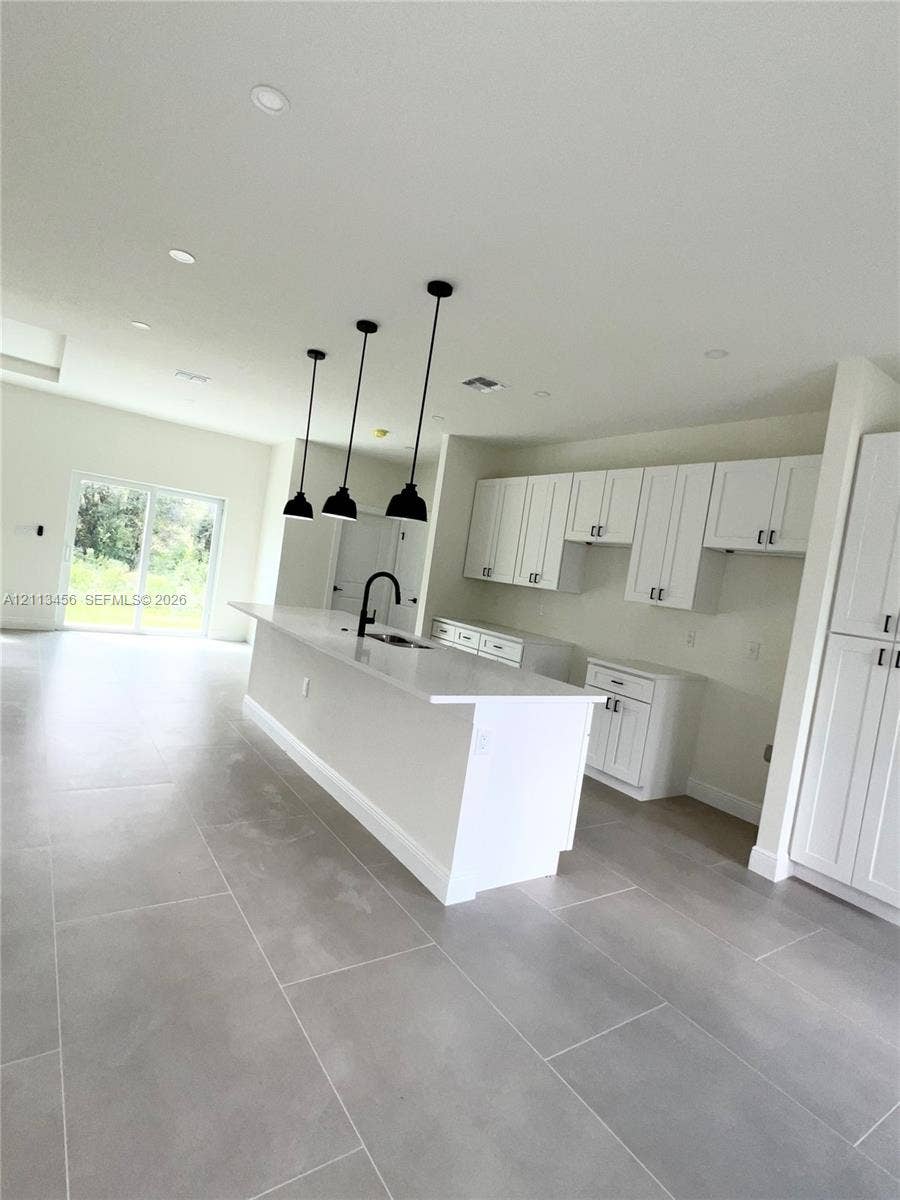 422 SE Eisenhower Boulevard, Lehigh Acres, FL 33974 Kitchen featuring white shaker-style cabinetry, quartz countertops, a central island with a matte black faucet, triple pendant lighting, and large-format tile flooring
