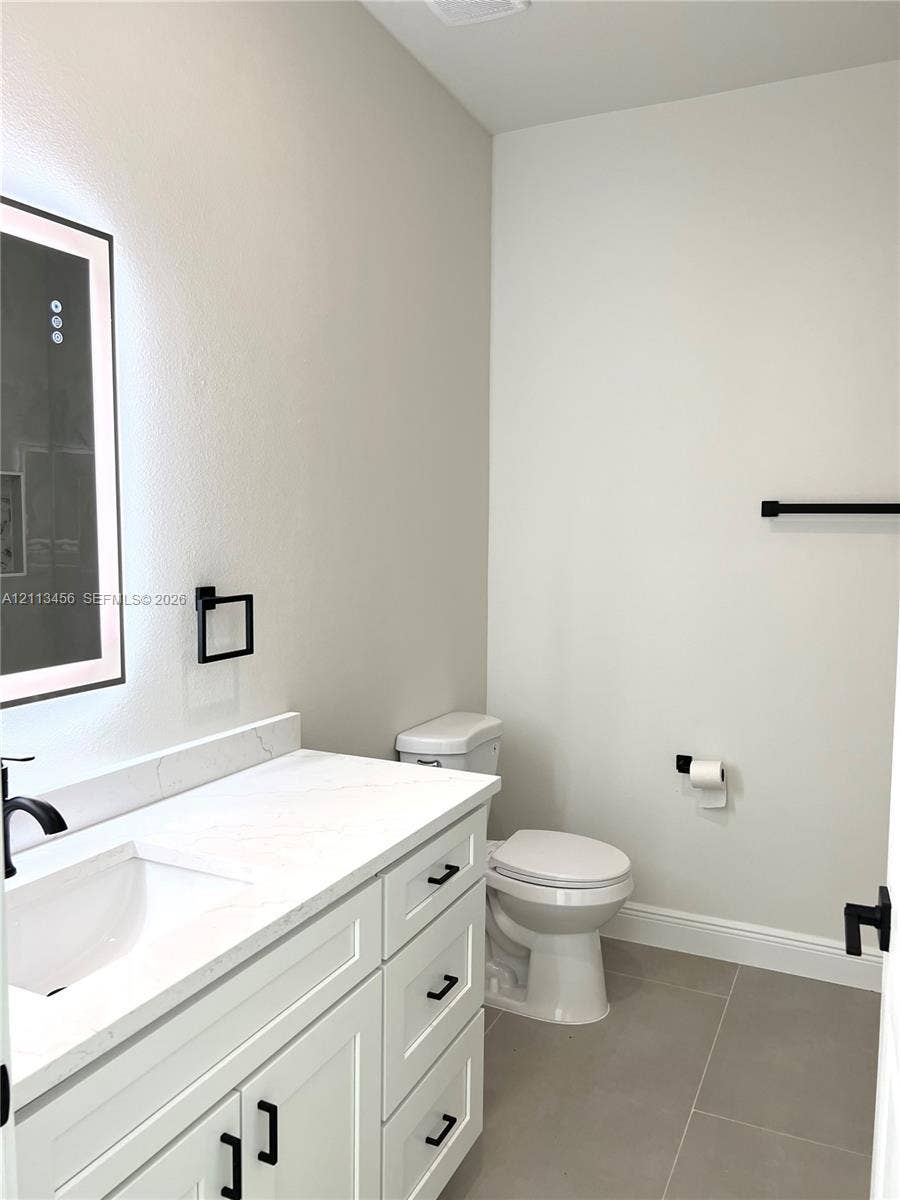 422 SE Eisenhower Boulevard, Lehigh Acres, FL 33974 White vanity cabinet featuring a quartz countertop, integrated rectangular sink, matte black hardware, and an illuminated wall-mounted mirror
