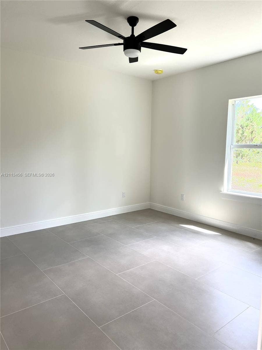 422 SE Eisenhower Boulevard, Lehigh Acres, FL 33974 Neutral-toned interior featuring large-format tile flooring, matte black ceiling fan with integrated lighting, and energy-efficient window