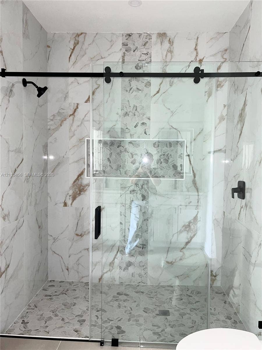 422 SE Eisenhower Boulevard, Lehigh Acres, FL 33974 Walk-in shower featuring large-format patterned wall tile, a vertical mosaic accent strip, pebble-stone flooring, a recessed wall niche, and a sliding glass door with matte black hardware