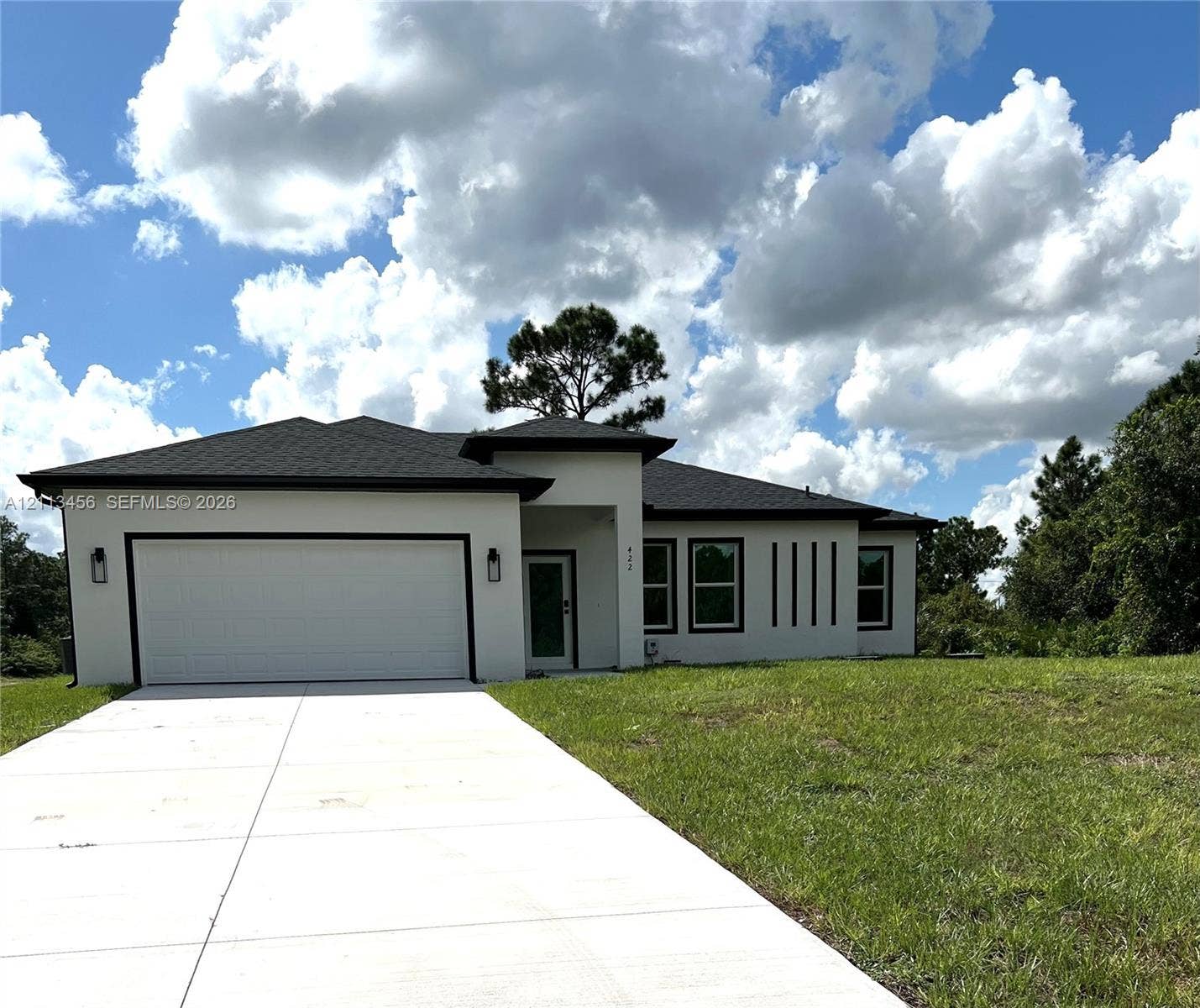 422 SE Eisenhower Boulevard, Lehigh Acres, FL 33974 Single-story stucco exterior featuring a hip roof, two-car garage, concrete driveway, and recessed entryway