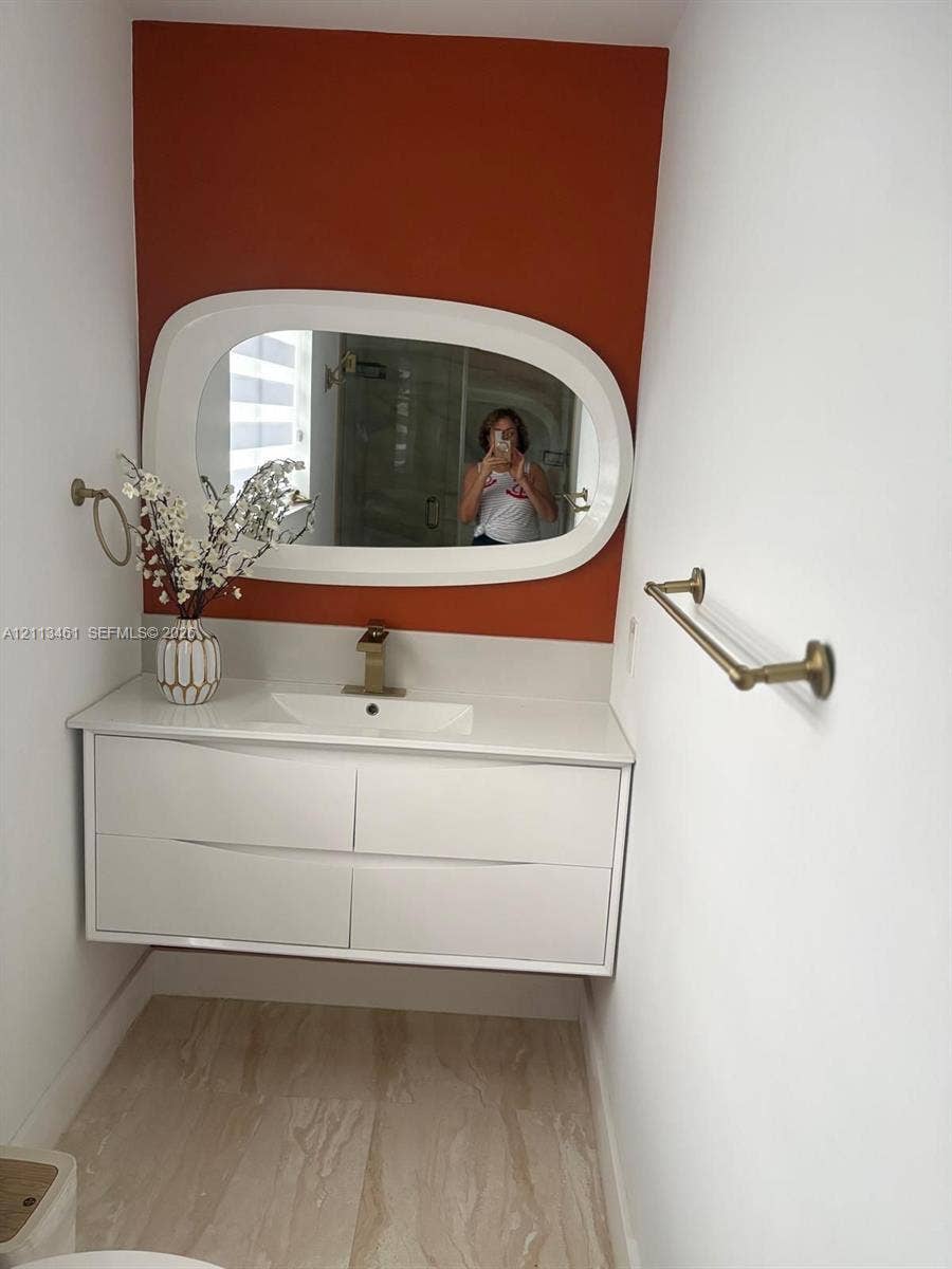 9961 SW 20th Street, Miami, Miami, FL 33165 Floating white dual-drawer vanity with an integrated countertop sink, matte gold single-handle faucet, oval-framed mirror, and gold-finish wall-mounted hardware